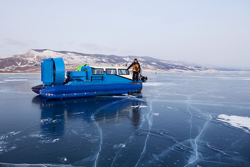 A man travels on a hovercraft on transparent ice with cracks in the frozen Lake Baikal. Kivus is a transport on ice. Winter trip.