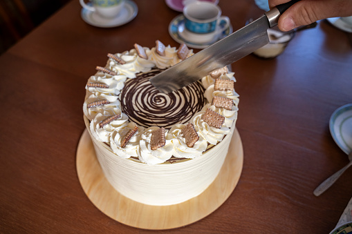 Close-up of a hand holding a knife and a layered cake being sliced.
