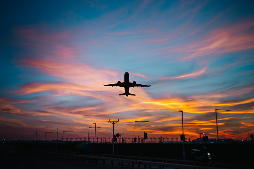 The dark silhouette of a climbing plane at sunset, below the airport lights.