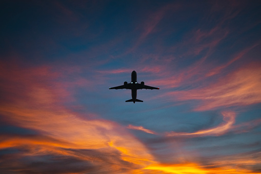 The silhouette of a passenger plane flying in sunset.