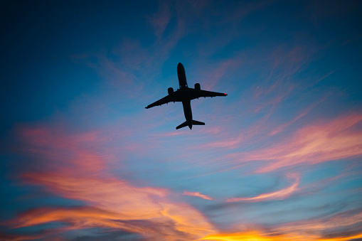 The dark silhouette of a climbing plane in the orange sky.