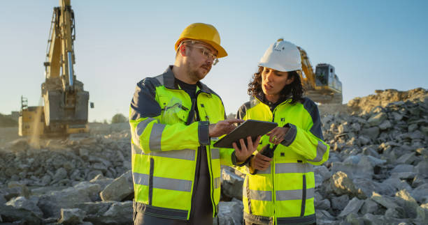 istock Caucasian Male Civil Engineer Talking To Hispanic Female Architect And Using Tablet On Construction Site of New Apartment Building. Real Estate Developers Discussing Business, Excavators Working. 1796831088