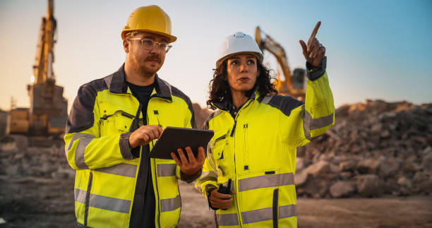istock Caucasian Male Civil Engineer Talking To Hispanic Female Inspector And Using Tablet Computer On Construction Site of New Building. Real Estate Developers Discussing Business, Excavators Working. 1796831102