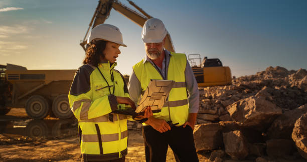 istock Caucasian Male Engineer And Hispanic Female Building Architect Walking On Construction Site With Laptop Computer And Talking About New Real Estate Project. Heavy Machinery Working. Golden Hour 1796834295