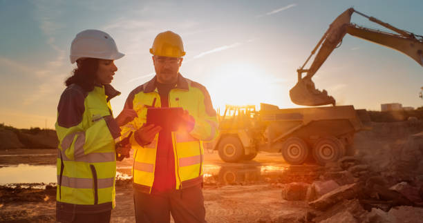 istock Caucasian Male Engineer Using Tablet And Talking To Hispanic Female Architect On Construction Site Of Real Estate Project. Colleagues Discussing Building Plan Of Apartment Complex During Golden Hour. 1796835009