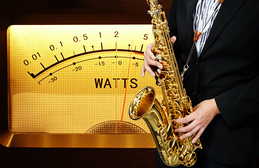 Male Musician in a Formal Black Suit Holds a Tenor Saxophone on Vu Meter background. Saxophonist Plays Jazz. Saxophone Close-up. Copy space.