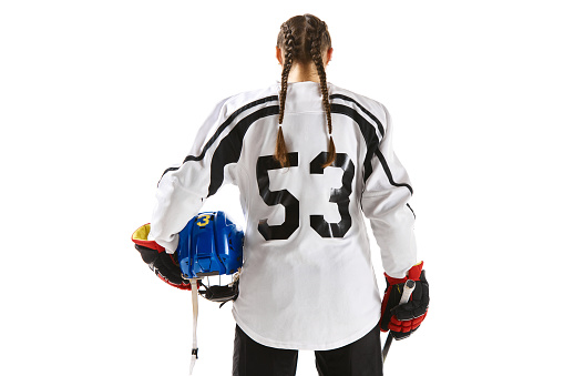 Young girl, hockey player in uniform standing with stick and posing isolated over white background. Back view. Concept of professional sport, competition, game, action, hobby, competition