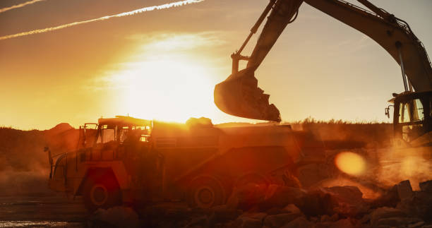 istock Construction Site On Sunny Evening: Industrial Excavator Loading Rocks Into A Truck. The Process Of Building Apartment Complex. Workers Operating Heavy Machinery To Complete A Real Estate Project. 1796842483