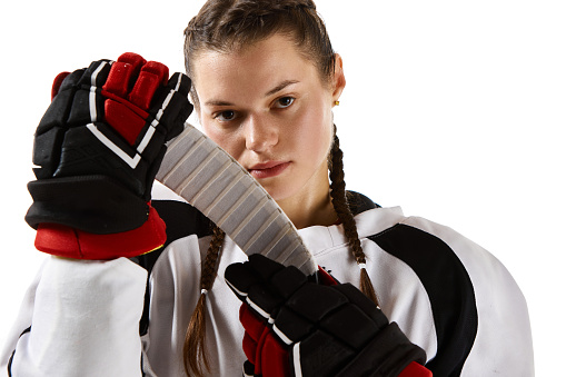 Portrait of young beautiful girl, hockey player in uniform standing with stick isolated over white background. Concept of professional sport, competition, game, action, hobby