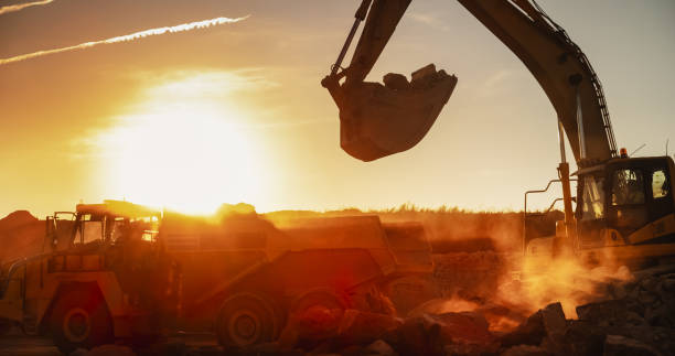 istock Construction Site On Sunny Evening: Industrial Excavator Loading Rocks Into A Truck. The Process Of Building New Apartment Complex. Workers Operating Heavy Machinery To Complete A Real Estate Project. 1796842505