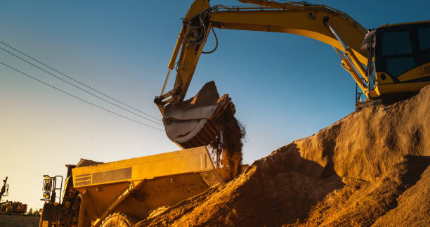 istock Construction Site On Sunny Evening: Industrial Excavator Loading Sand Into A Truck. The Process Of Building a New Apartment Complex. Workers Operating Heavy Machinery To Complete A Real Estate Project 1796842508