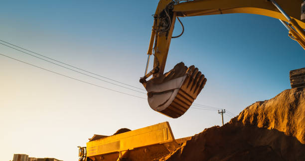 istock Construction Site On Sunny Evening: Industrial Excavator Loading Sand Into A Truck. The Process Of Building a New Apartment Complex. Workers Operating Heavy Machinery To Complete Real Estate Project 1796843012