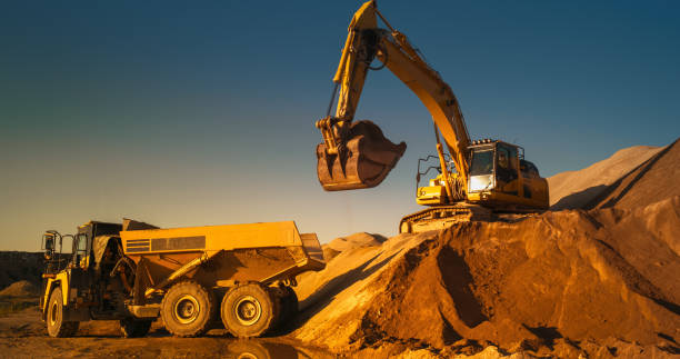 istock Construction Site On Sunny Evening: Industrial Excavator Loading Sand Into A Truck. The Process Of Building New Apartment Block. Workers Operating Heavy Machinery To Complete A Real Estate Project. 1796843024