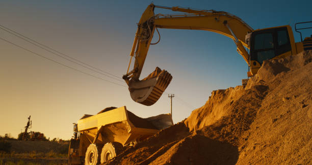 istock Construction Site On Sunny Evening: Industrial Excavator Loading Sand Into A Truck. The Process Of Building New Apartment Block. Workers Operating Heavy Machinery To Complete New Real Estate Project. 1796843033
