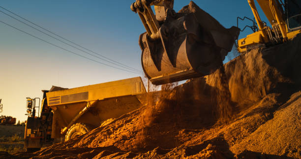 istock Construction Site On Sunny Evening: Industrial Excavator Loading Sand Into A Truck. The Process Of Building New Apartment Complex. Workers Operating Heavy Machinery To Complete A Real Estate Project. 1796843573