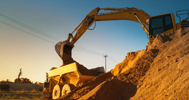 istock Construction Site On Sunny Evening: Industrial Excavator Loading Sand Into A Truck. The Process Of Building New Apartment Complex. Workers Operating Heavy Machinery To Complete New Real Estate Project 1796844083