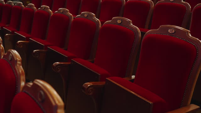 Soft rich rows of red wooden chairs in auditorium of classical theater.