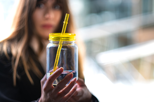 Modern sip: Brown-haired girl holds trendy shake bottle, corporate setting, stylish ambiance.