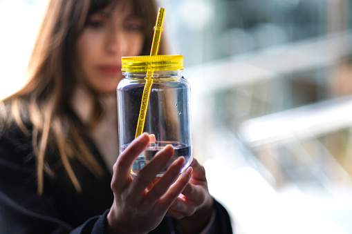 Milkshake bottle with straw held by a blurred young woman in Madrid, business background.