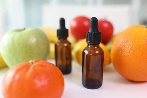 A bottle with a pipette on a table with fruits and vegetables, a close-up. Organic citrus oil, natural ingredient