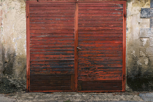 Red wooden double doors and worn out cement wall of an antique building.