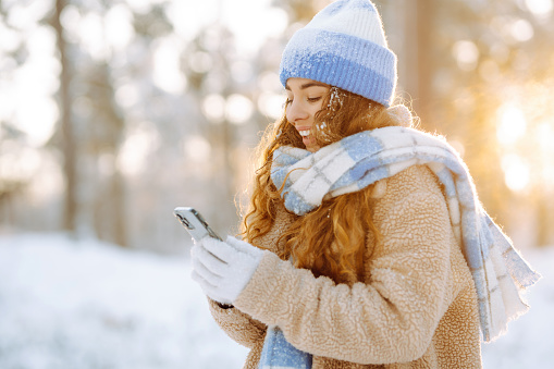 A young woman in a snowy park with a phone in her hands communicates via video and takes a selfie.