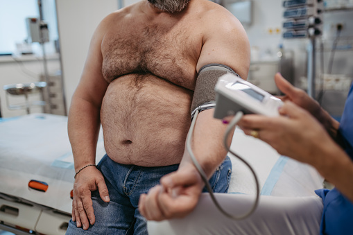 Doctor measuring blood pressure, examining hypertension, using blood pressure monitor. Obesity affecting middle-aged men's health. Concept of health risks of overwight and obesity.