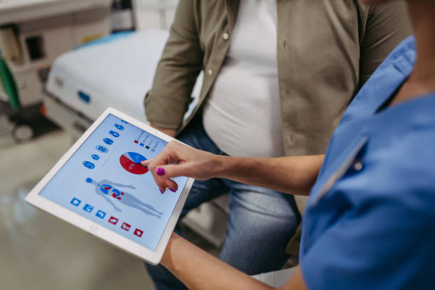 Gros plan d’une femme médecin consultant un patient en surpoids, discutant du résultat du test dans le cabinet du médecin. Affichage du rapport médical sur tablette. L’obésité affecte la santé des hommes d’âge moyen. Concept des risques pour  - Photo