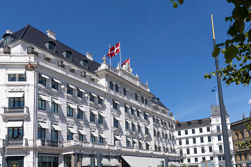 The most luxurious Hotel D'Angleterre in Copenhagen with Danish flags on a summer sunny day. Copenhagen, Denmaerk - July 26, 2023