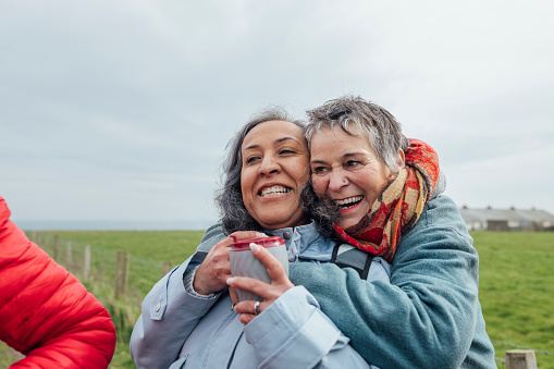 Two mature women enjoying a day out in Howick, North East England. They are enjoying a walk in the fresh air together, taking a break from walking and one woman has her arms around her friend while they both laugh and smile.

Videos also available for this scenario.