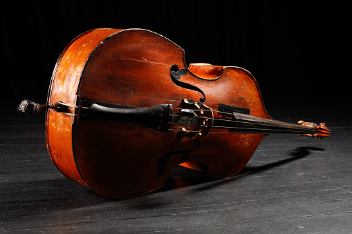 Wooden musical string instrument on a black floor of stage.  Double bass bridge and strings. Contrabass in a dark. Shallow depth of field