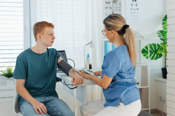 Doctor measuring boy's blood pressure, using blood pressure monitor. Teenage boy visiting paediatrician for annual preventive physical examination. Concept of preventive health care for adolescents. Doctor, nurse measuring boy's blood pressure, using blood pressure monitor. Teenage boy visiting paediatrician for annual preventive physical examination. Concept of preventive health care for adolescents. sports physical stock pictures, royalty-free photos & images
