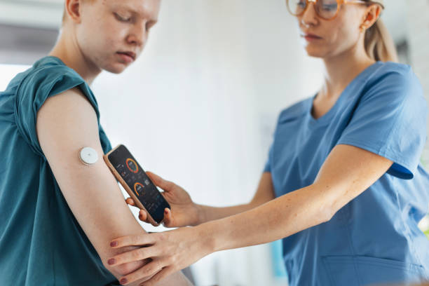Diabetologist doctor connecting continuous glucose monitor sensor to smartphone, checking teenage boy's glucose data in real time. Endocrinologist taking care of teenage diabetic patient. stock photo