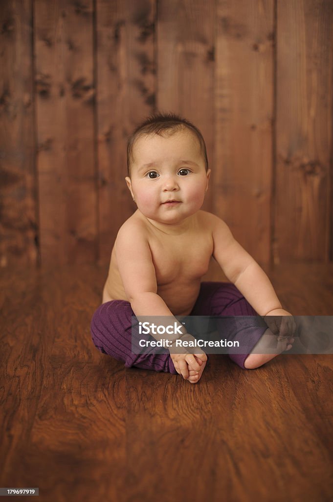 Baby Girl Sitting on Wood Floor A baby girl wearing purple leggings and sitting on a wood floor. Baby - Human Age Stock Photo