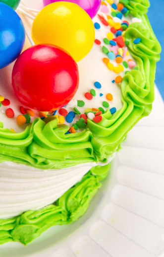 Closeup of white birthday cake green icing trim and multi-color sprinkles and colored balls