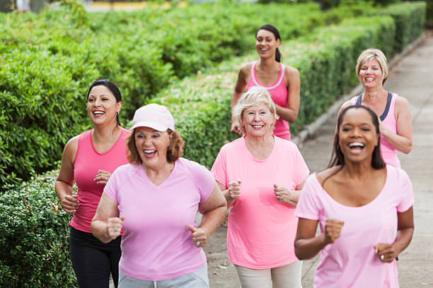 Breast cancer rally Multi-ethnic group of women (30s, 40s, 60s) wearing pink, participating in breast cancer rally. Main focus on Hispanic woman (30s) on left, and senior woman (60s) looking at camera. walking for a cause stock pictures, royalty-free photos & images