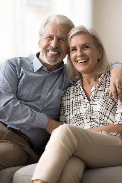 веселые позитивные пожилые пенсионеры муж и жена обнимаются на диване - middle human age couple women стоковые фото и изображения