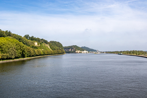Panoramic view of Albert canal, rocky mountains with lush green trees in Belgian part of Sint-Pietersberg, Lanaye locks in background, sunny summer day in Ternaaien, Liege province, Belgium