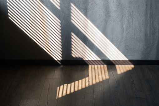 Light and shadow from the window. Thin lines of light on the wall and floor. The texture of the plaster. Shadow from the blinds.