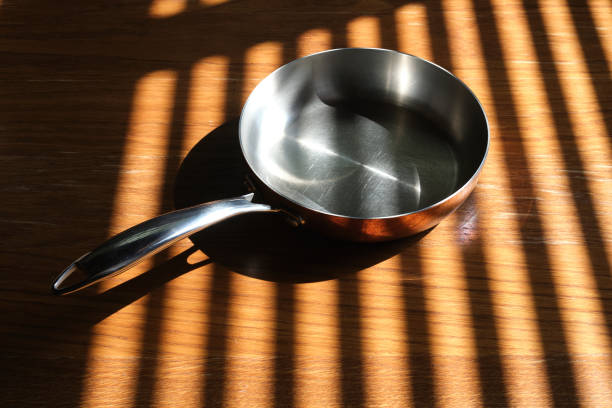 istock Empty pan with a copper coating on a wooden table. Light and shadow from the window. 1797052024