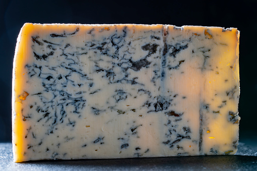 Piece of blue cheese on dark background, close up