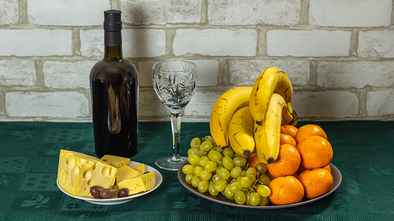 On the table is a bottle of wine, a platter of fruit and cheese