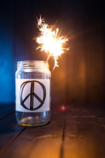 Hope for peace, still life with glass jar with peace symbol and burning sparkler. Background with copy space. Vertical shot.