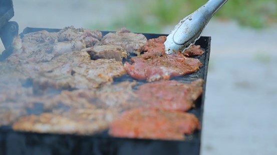 Barbecue outdoors. Grilling a raw meat steak on a burning fire, a man uses tongs to flip a grilled steak on a barbecue grill. Close-up of a delicious grilled meat steak.