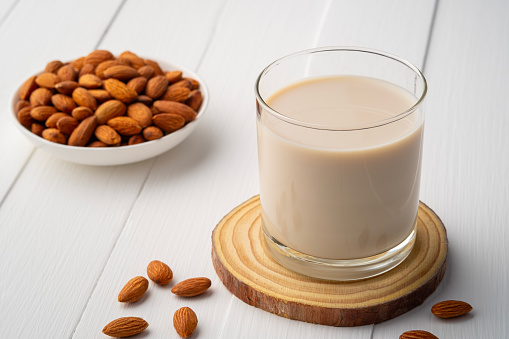 Almond milk in the glass with almond on wooden plate.