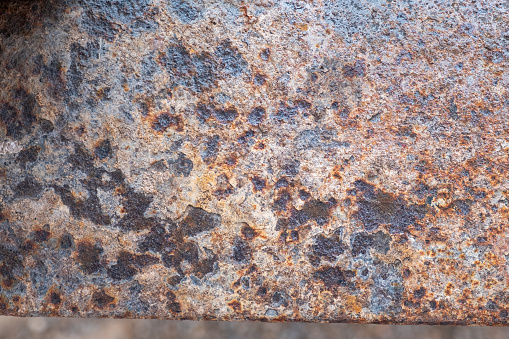 Detail of a rusty sheet of metal with a splotchy, multicolored surface, pock marked and grungy from the corrosion of the rust.