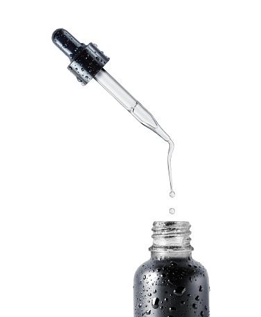 Stretched drop dripping from a cosmetic pipette isolated on a white background. Black bottle with cosmetic oil close up