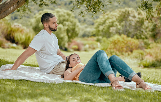 Love, couple and relax on blanket in park, nature or \noutdoors bonding and resting. Romance, support and woman sleeping outside with man by tree, enjoying date or vacation time together in garden.