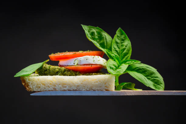 fresh slice of bread with pesto sauce, mozzarella and tomato on a wooden spatula with basil. stock photo