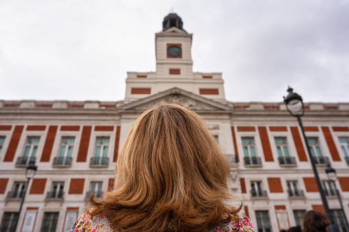 Tourist woman with her back looking at the clock tower of the Puerta del Sol buildings in Madrid